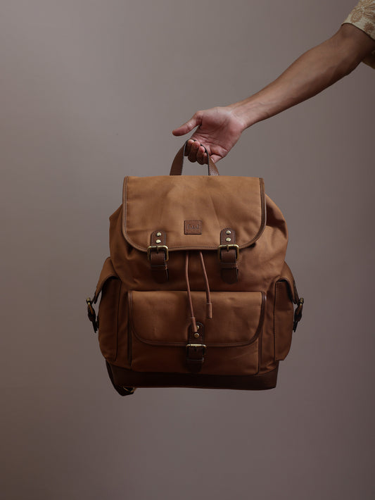 Explorer Series tan canvas and reclaimed leather drawstring travel backpack with flap closure, antique brass buckles, front utility pockets, and leather trim, held by hand.