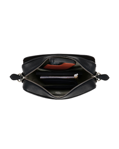 Top view of the Studio Ek Inch Metropolitan crossbody bag showing organized compartments for a smartphone, wallet, notebook, charger and everyday essentials. Crafted from waterproof canvas and reclaimed leather for modern travel.